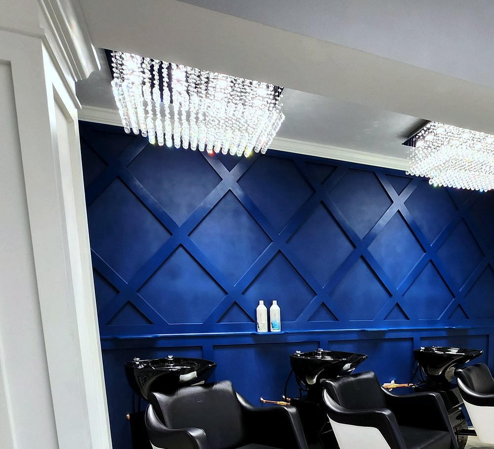 Navy quilted accent wall with crystal chandelier above the shampoo stations